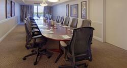 Water Pitchers, Drinking Glasses, Notepads, and Ergonomic Chairs at Boardroom Table in Executive Suite With Wall Art, and Window With Open Drapes 
