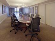 Water Pitchers, Drinking Glasses, Notepads, and Ergonomic Chairs at Boardroom Table in Executive Suite With Wall Art, and Window With Open Drapes 