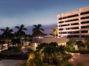 Illuminated Hotel Exterior, Signage, Palm Trees, Landscaping, and Cars on Parking Lot at Dusk