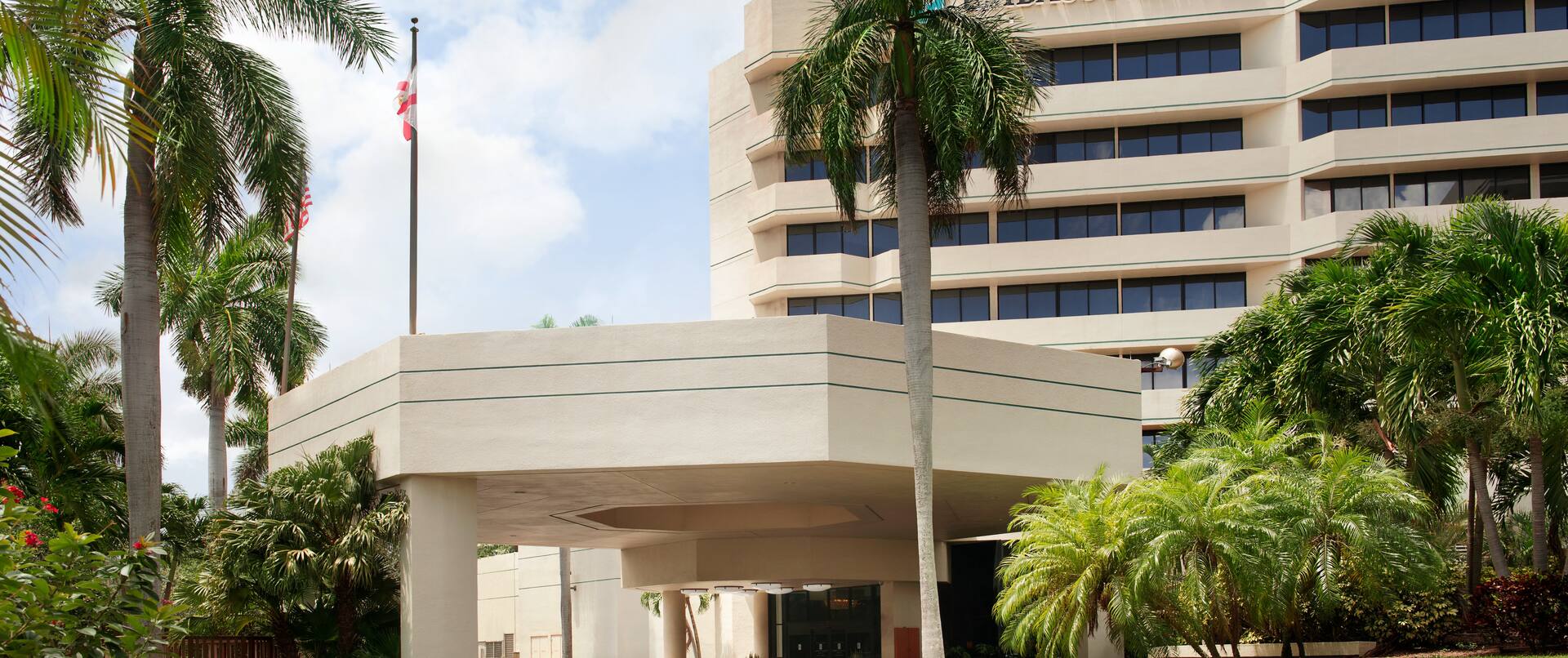 Daytime View of Hotel Exterior, Signage, Flagpole, Landscaping, and Porte Cochère