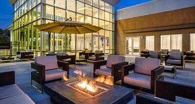 Table With Umbrella and Lounge Seating Around Patio Fire Pit at Night