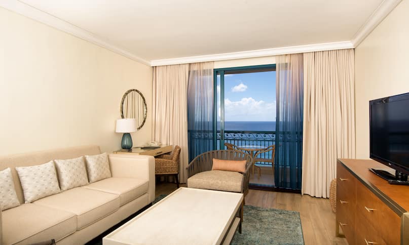 Suite with lounge sofa, chair, coffee table, TV, and outdoor patio balcony with ocean view