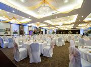 Ballroom With White Chairs, Place Settings, Flowers, and White Linens on Banquet Tables