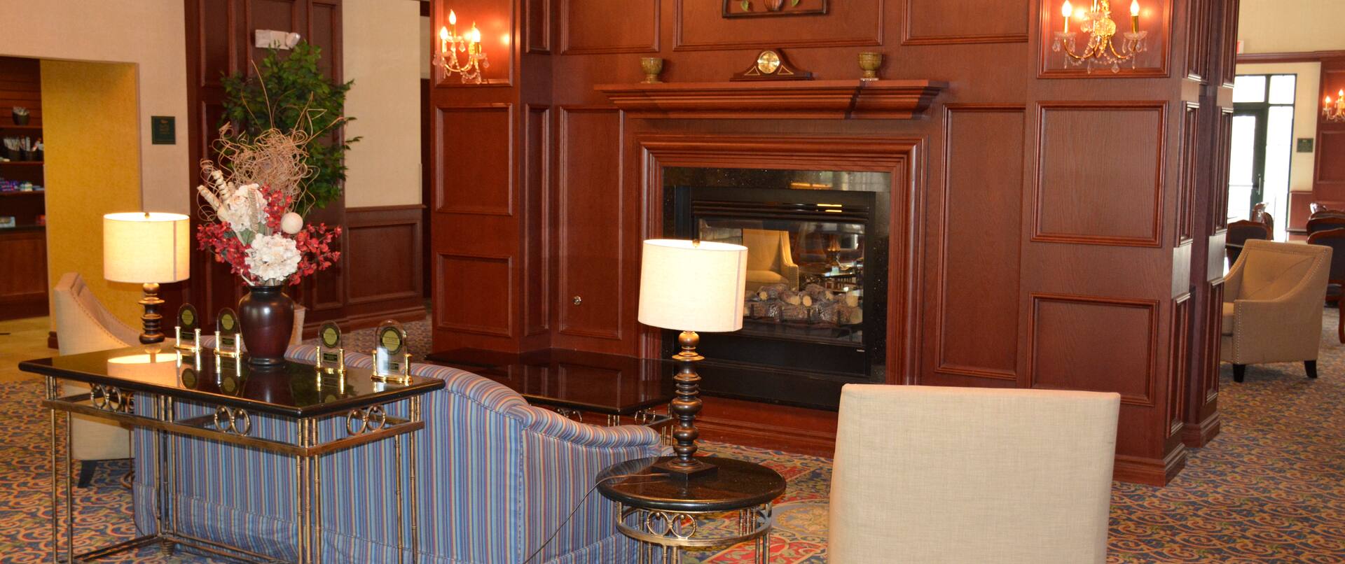 Two Armchairs, Sofa, and Tables With Illuminated Lamps Around Fireplace in Lobby Lounge Area