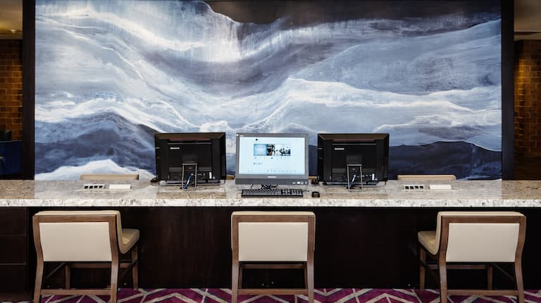 Business Center With Three Computers on Large Work Desk and Chairs in Front of Brightly Lit Wall Mural