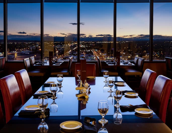 Detailed View of Place Settings On Dining Table by Window With Dusk View of Illuminated City