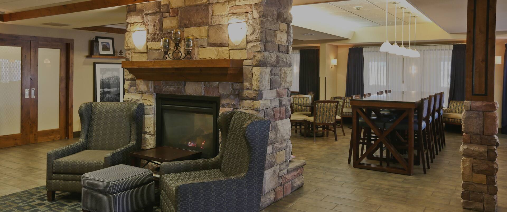 Lobby dining area with high-top table, high chairs, soft chairs, ottoman, and fireplace
