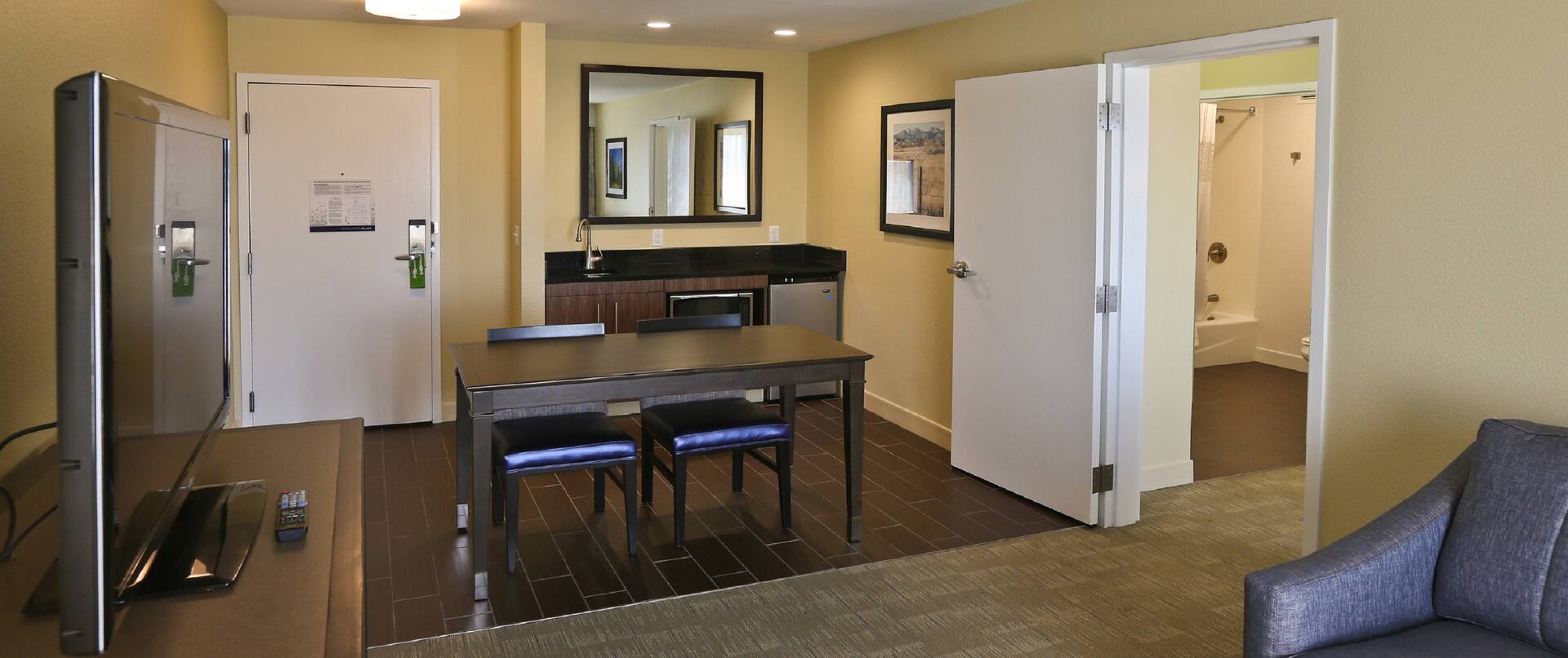 Suite living area with dining table, chairs, wet bar, TV, room entrance, and partial view of lounge sofa