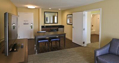 Suite living area with dining table, chairs, wet bar, TV, room entrance, and partial view of lounge sofa