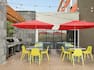 Beautiful outdoor patio featuring tables with chairs, red umbrellas, string lights, and BBQ grills.