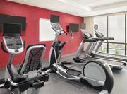 Bright fitness center featuring floor to ceiling windows, various types of cardio machines, and TVs.