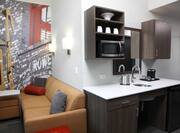 Wall Mural, Sofa, Ottoman, and Hospitality Center With Drinkware in Overhead Cabinets, Microwave, Sink, Mini Fridge