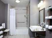 Fresh Towels, Shower Seat, Accessible Bathtub With Grab Bars, and Handheld Showerhead, Large Vanity Mirror, Sink, and Toiletries in ADA Guest Bath
