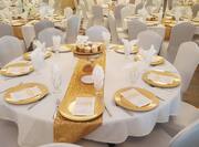 Detailed View of Round Wedding Event Tables With Gold Decorations, Place Settings, and Tray of Cupcakes on White Linens, and White Chair Set Up for a Wedding