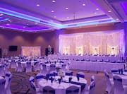 Wedding Reception Setup in Meeting Room With Purple and White Lighting, Place Settings, Flowers, and Purple Decor on Tables With White Linens
