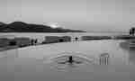 Person Swimming in the Infinity Pool with Coast View at Sunset