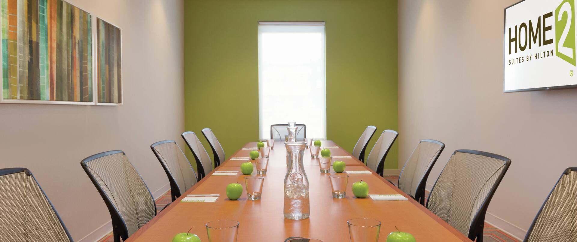 Boardroom with long table set with pens, paper, water glasses, and green apples