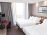 Hotel Guest Room with Two Double Beds, TV, Desk and Large Window letting Natural Light In