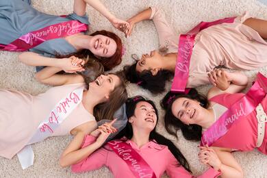 Group of bridesmaids and bride lying on a carpeted floor holding hands