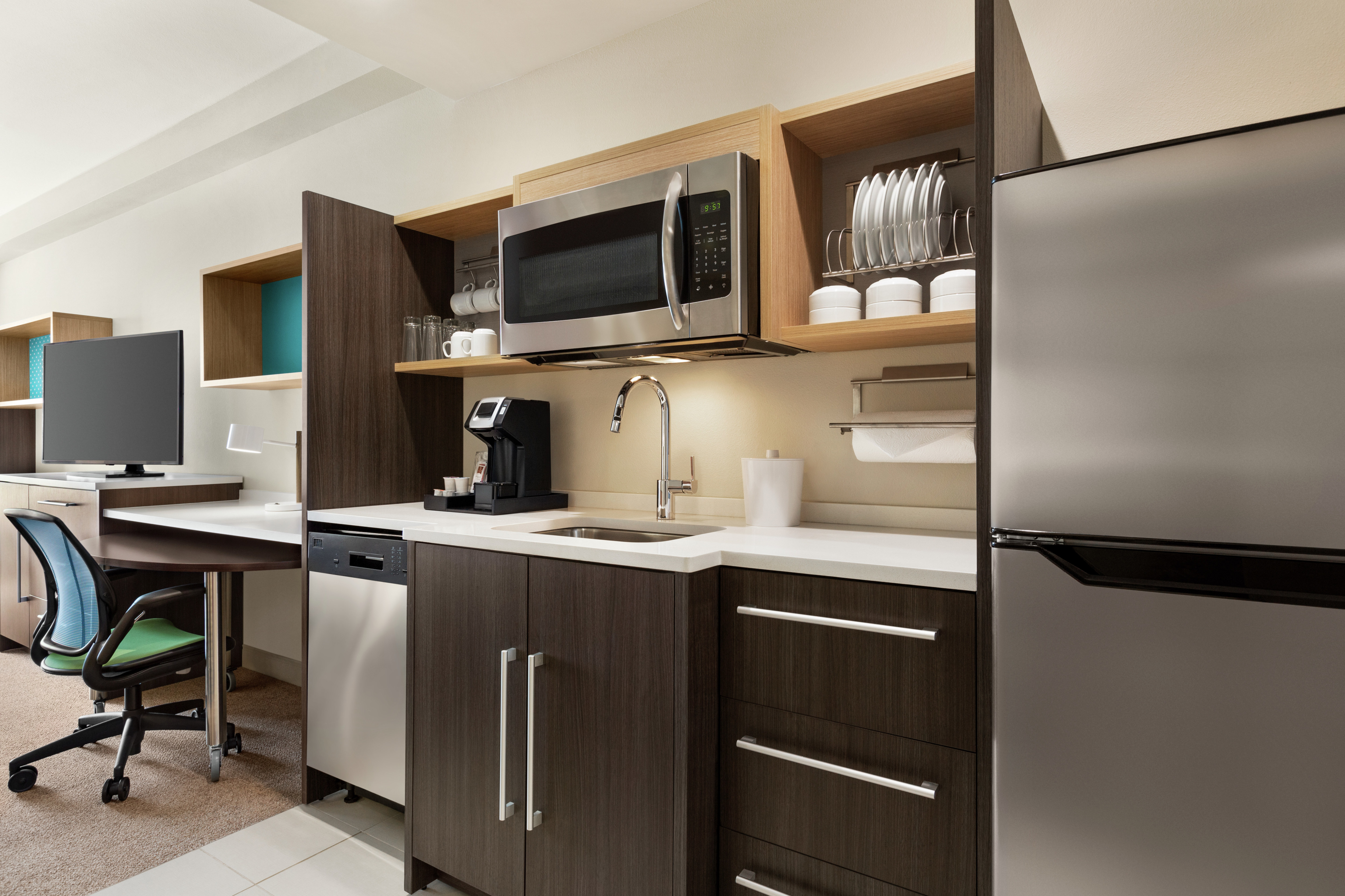 Bright studio suite featuring fully equipped kitchen, work desk, and TV.