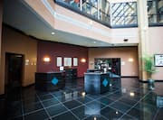 Vast Lobby With Dark Tile Floor, Wall Art Behind Three Reception Stations and View of Second Floor