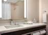 Shower Curtain Reflected in Brightly Lit Vanity Mirror, Sink, Fresh Towels, Toiletries and Amenities in Standard Bathroom