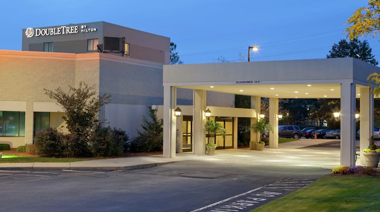 Angled View of Hotel Exterior, Signage, Porte Cochere, Landscaping, and Guest Cars on Parking Lot Illuminated at Night
