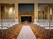 Wedding Ceremony Setup With Rose Petals on White Aisle Leading to Altar at Fireplace Surrounded by White Chairs
