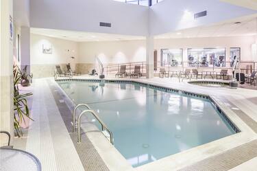 Tables and Chairs Around Indoor Pool and Whirlpool With Skylight and View Into Fitness Center