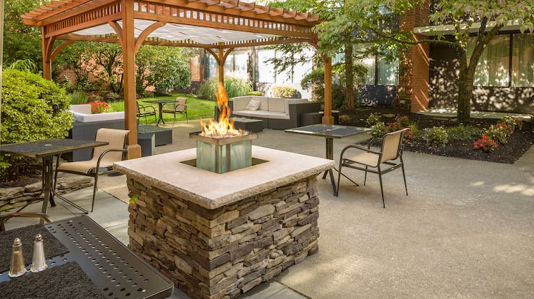  Tables and Chairs Around Fire Pit and Pavilion on Hotel Exterior Patio Surrounded by Trees
