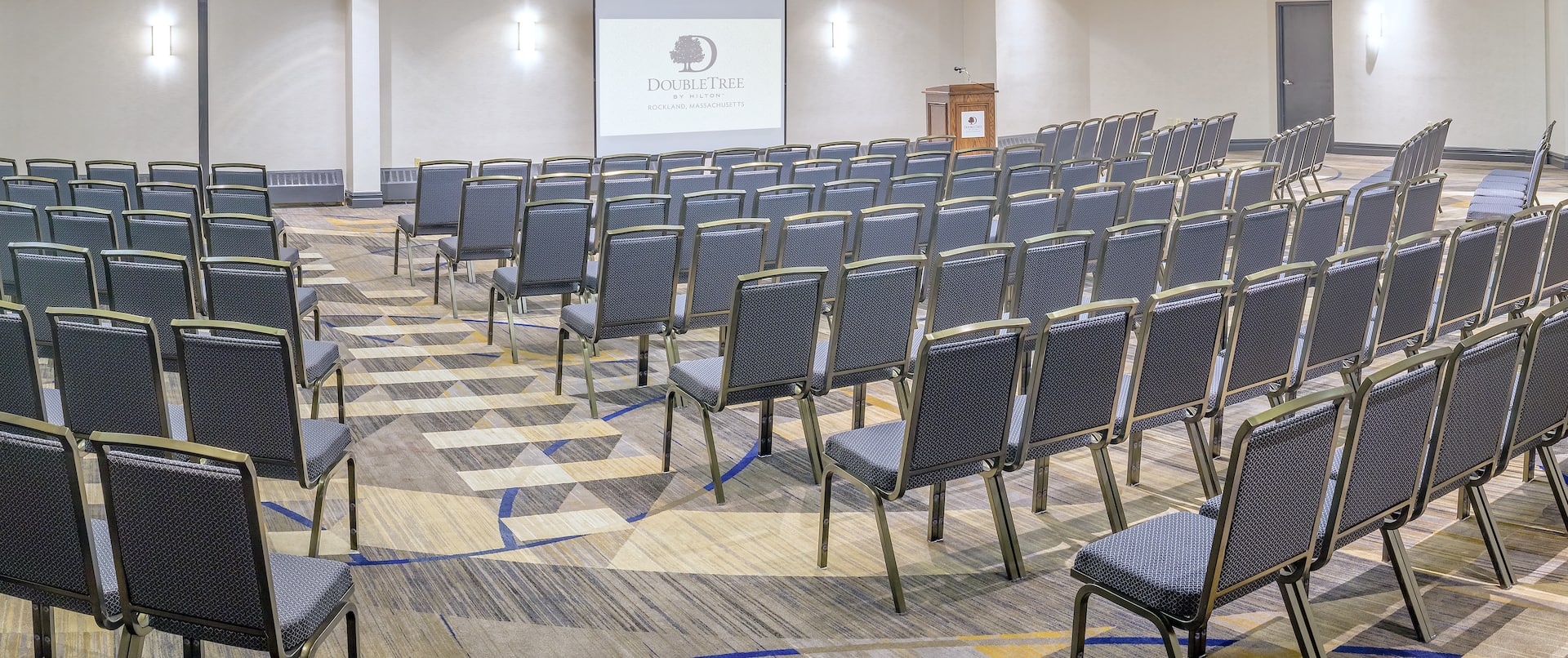 Meeting Room Arranged Theater Style With Rows of Chairs Facing Projector Screen and Podium