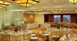 Ballroom Set Up for Wedding Reception With Head and Cake Tables By Dance Floor, Place Settings, and Flowers on Round Tables With Gold Linens and Chairs
