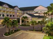 Beautiful Hilton Garden Inn hotel featuring lush palm trees, guest room balconies, and dusk sky.