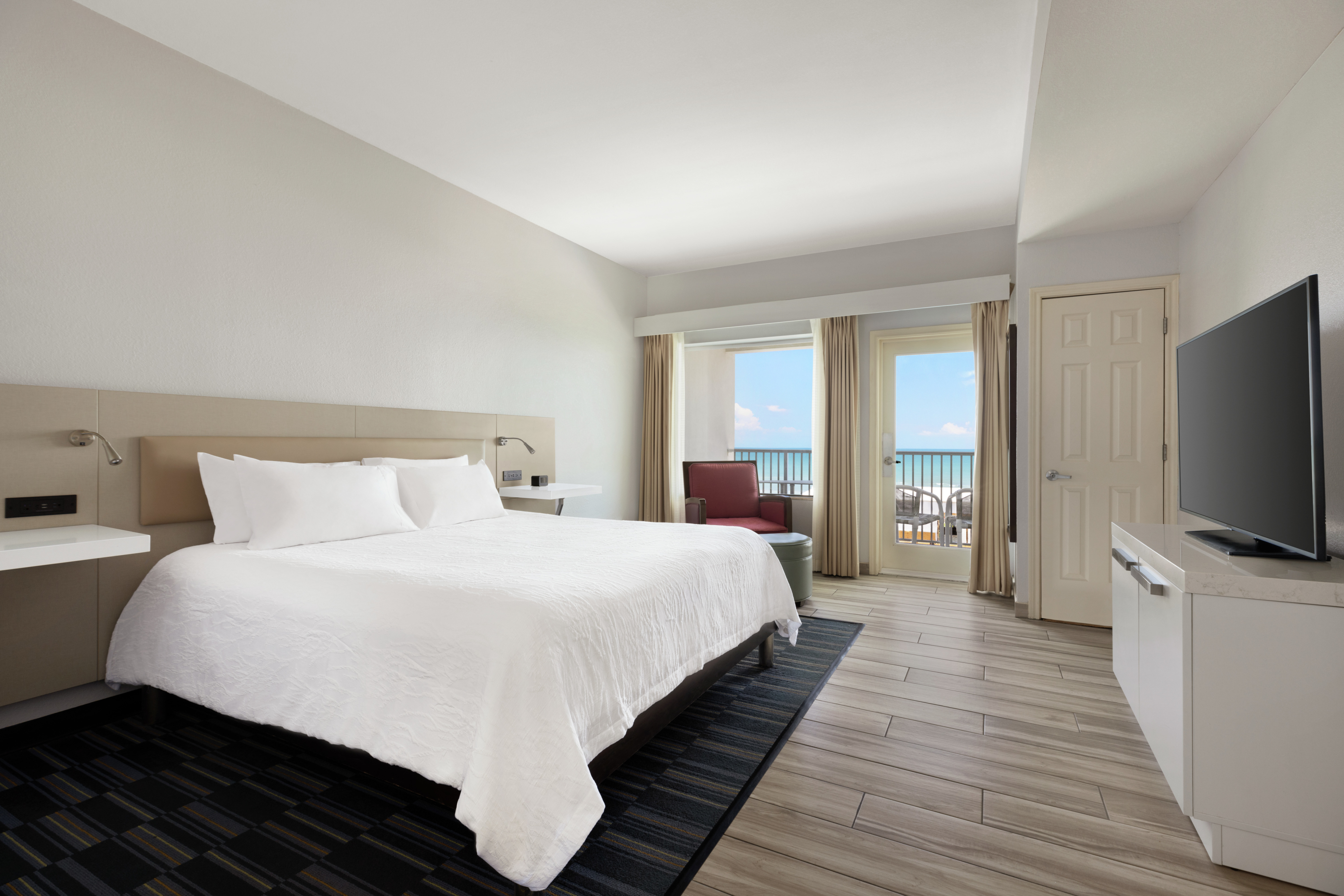 Spacious guest room featuring comfortable king bed, TV, and stunning ocean view.