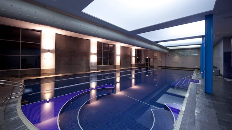 Night Time View of Illuminated Indoor Pool With Large Windows 