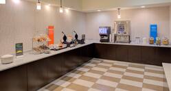 Breakfast serving area with waffle station, coffee, juice, cereals, pastries, and dining amenities
