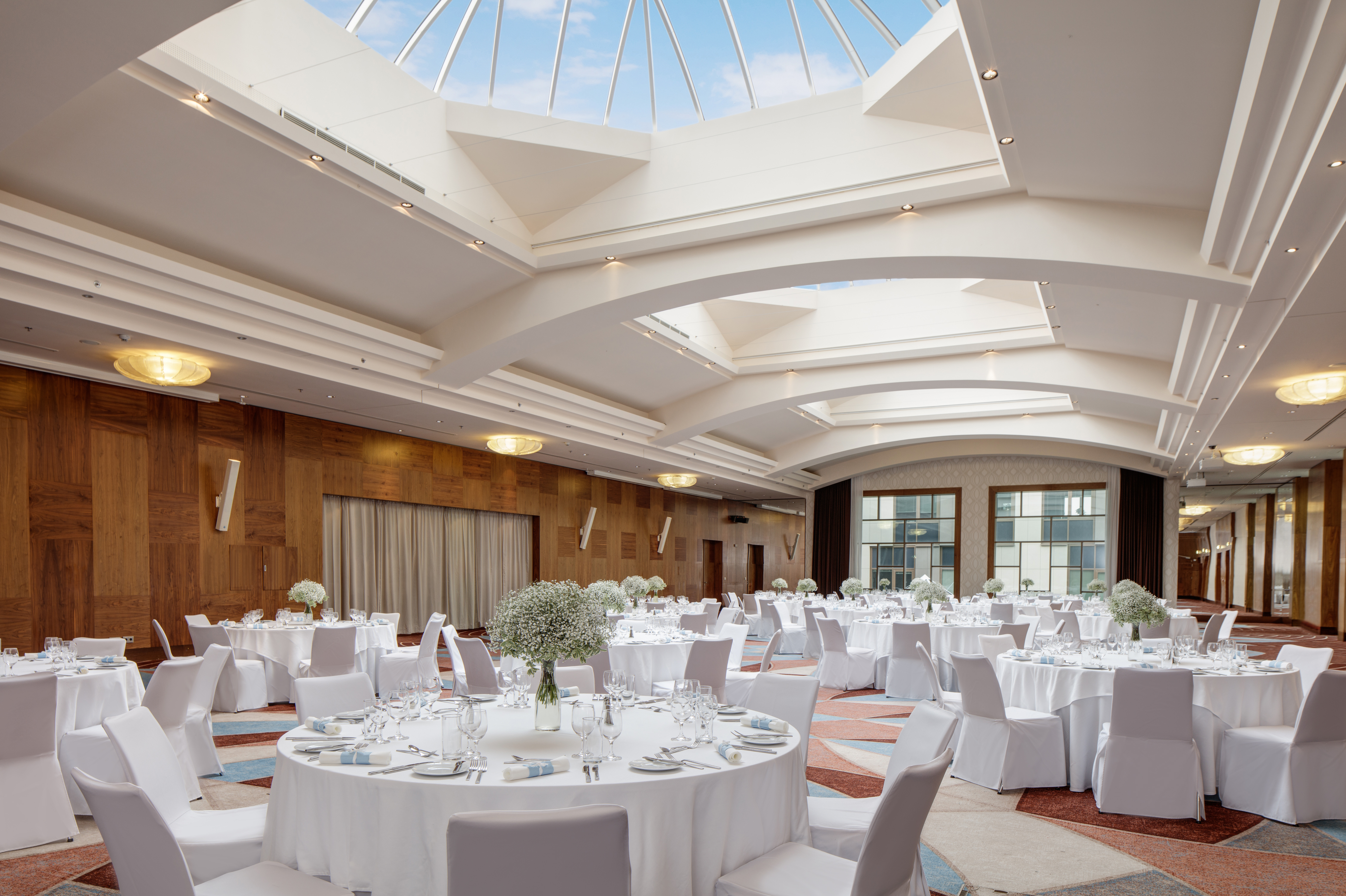 Place Settings and Flowers on Round Dining Tables With White Linens in Hilton Ballroom With Sky Lights