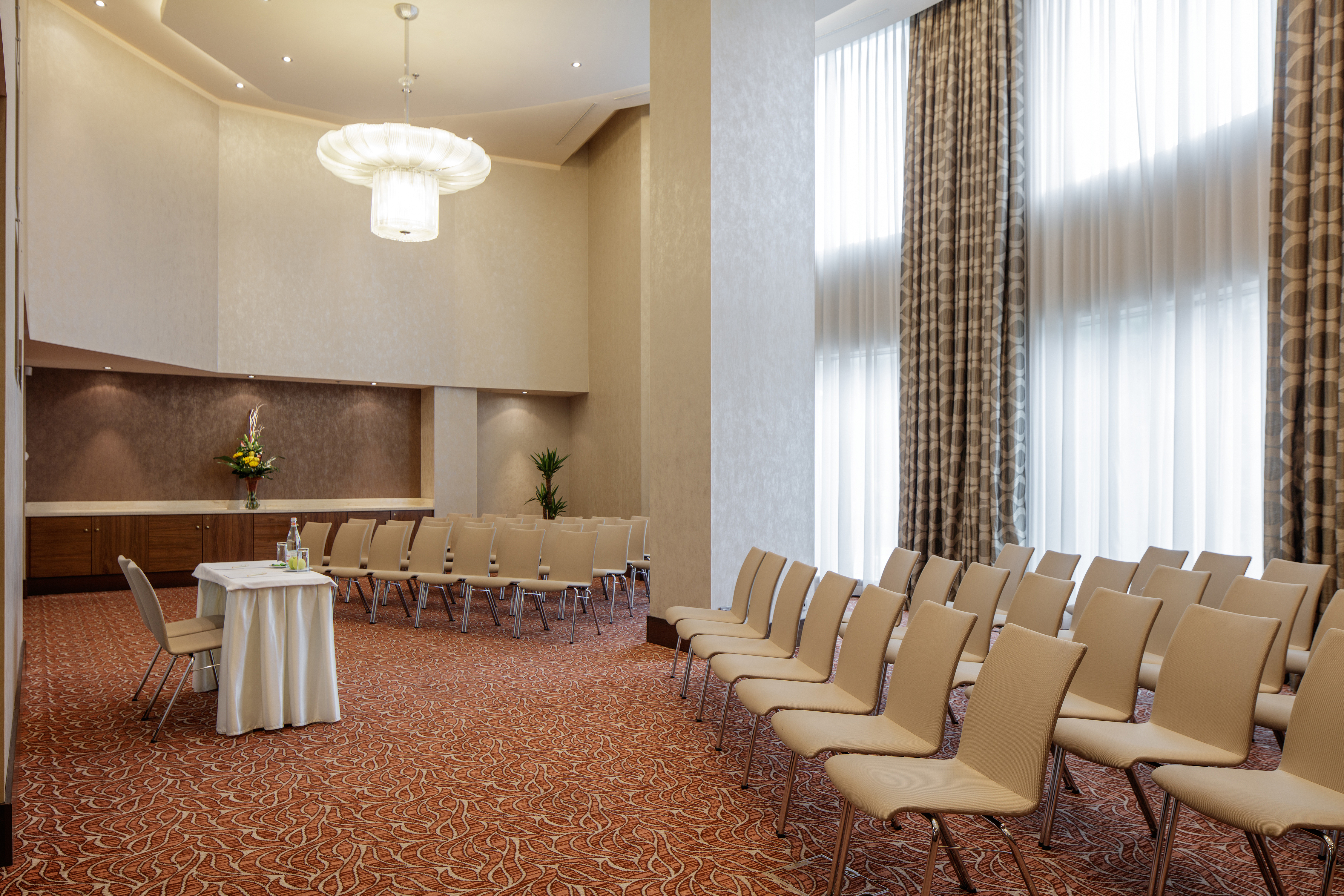 Long Sheer Drapes on Windows in Room Foyer Arranged Theater Style With Rows of Chairs Facing Speaker's Table and Chair