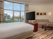 King Bed Window With Open Drapes and City View, TV, Wall Art, Sofa, Coffee Tables, and Floor Lamp in Deluxe Room