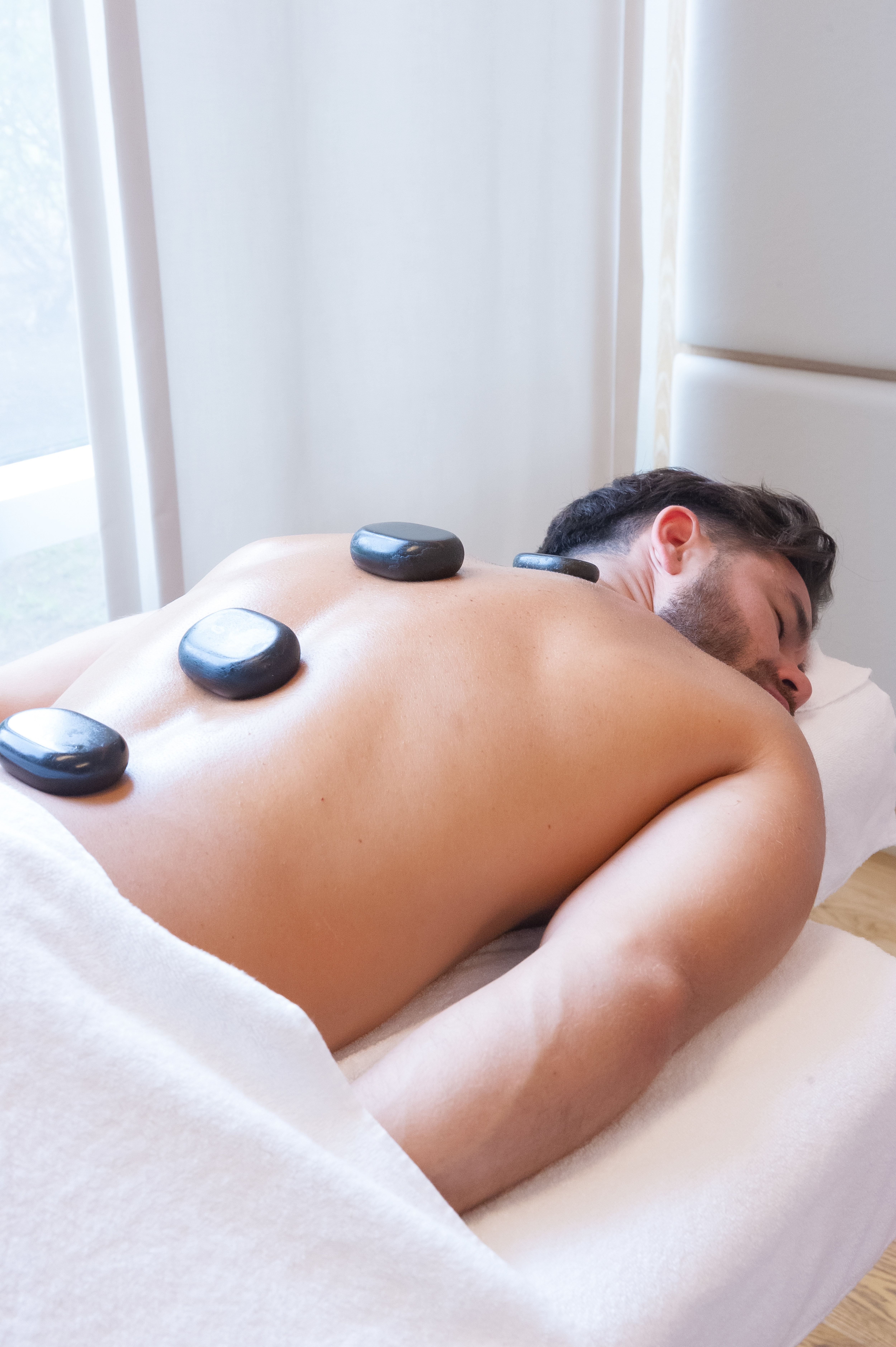 Hombre recibiendo un masaje con piedras calientes en el spa