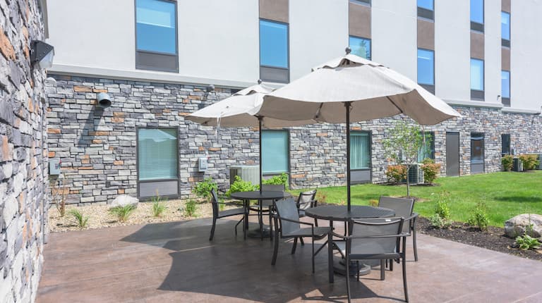 Two Patio Tables with Three Chairs and One Umbrella at Each  with view of Building Exterior and Landscaping