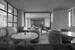 Restaurant with upholstered chairs, round tables, table lamps, and large windows