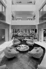 Hotel lounge with curved chairs, round tables, a long sofa, and a tall atrium ceiling
