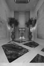Hotel entry hall with patterned stone floor, tall potted trees, curtains, and glass doors