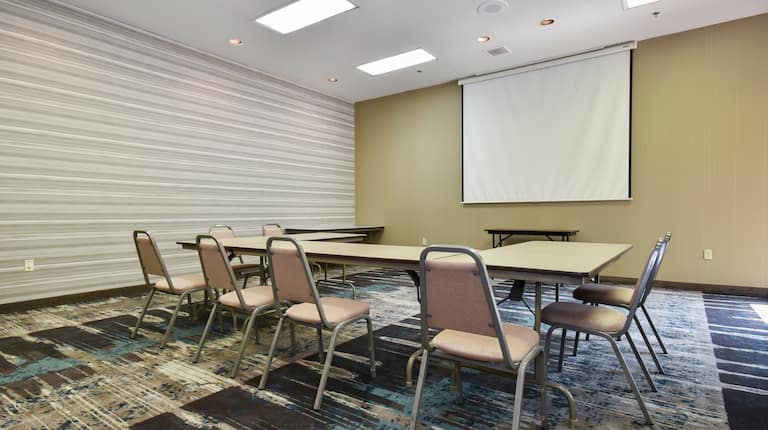 Meeting room with long table and multiple chairs and projector screen.