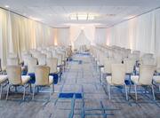 Meeting Room Arranged Theater Style Surrounded by Sheer Drapes With Rows of White Chairs Facing Table Under Draped Archway