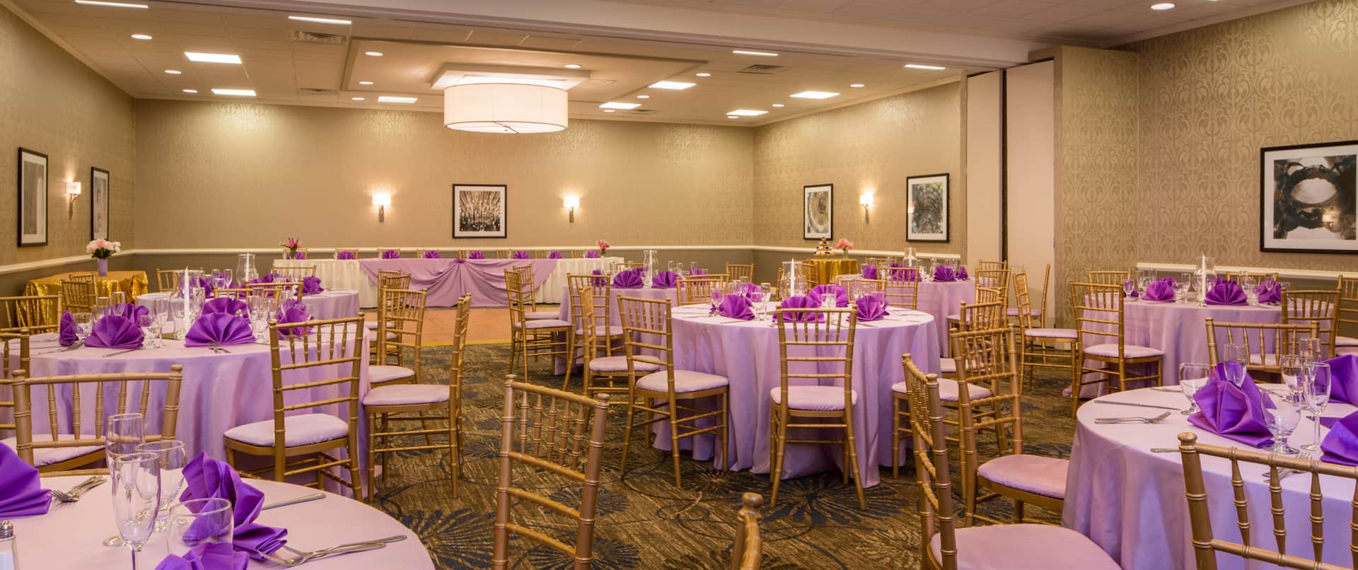 Round Tables With Place Settings, Purple Napkins, and Candles on White Linens, Dance Floor, and Head Table in Event Space
