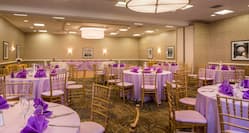 Round Tables With Place Settings, Purple Napkins, and Candles on White Linens, Dance Floor, and Head Table in Event Space