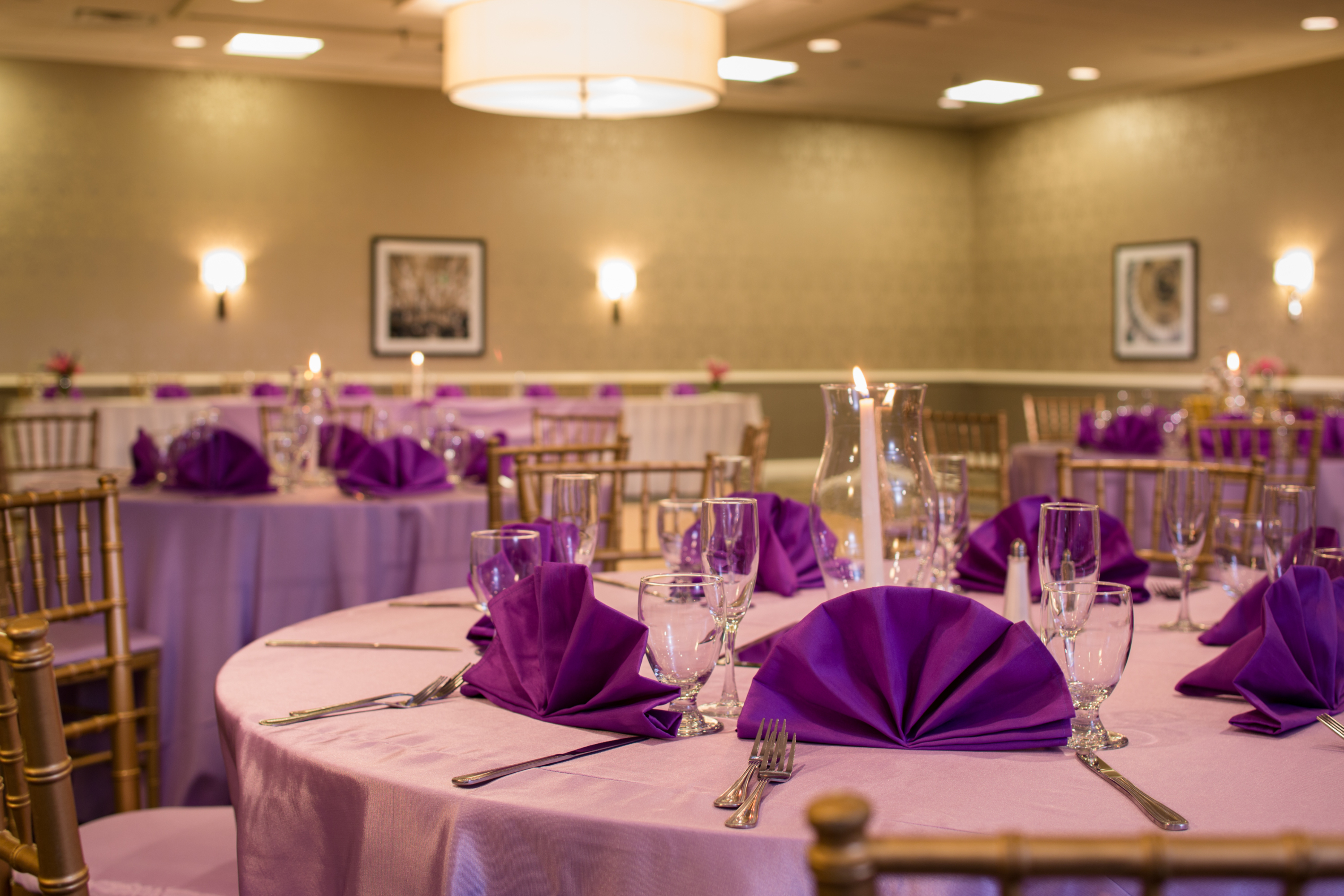 Place Settings, Purple Napkins, and Candles on Round Tables With White Linens Set Up for a Wedding
