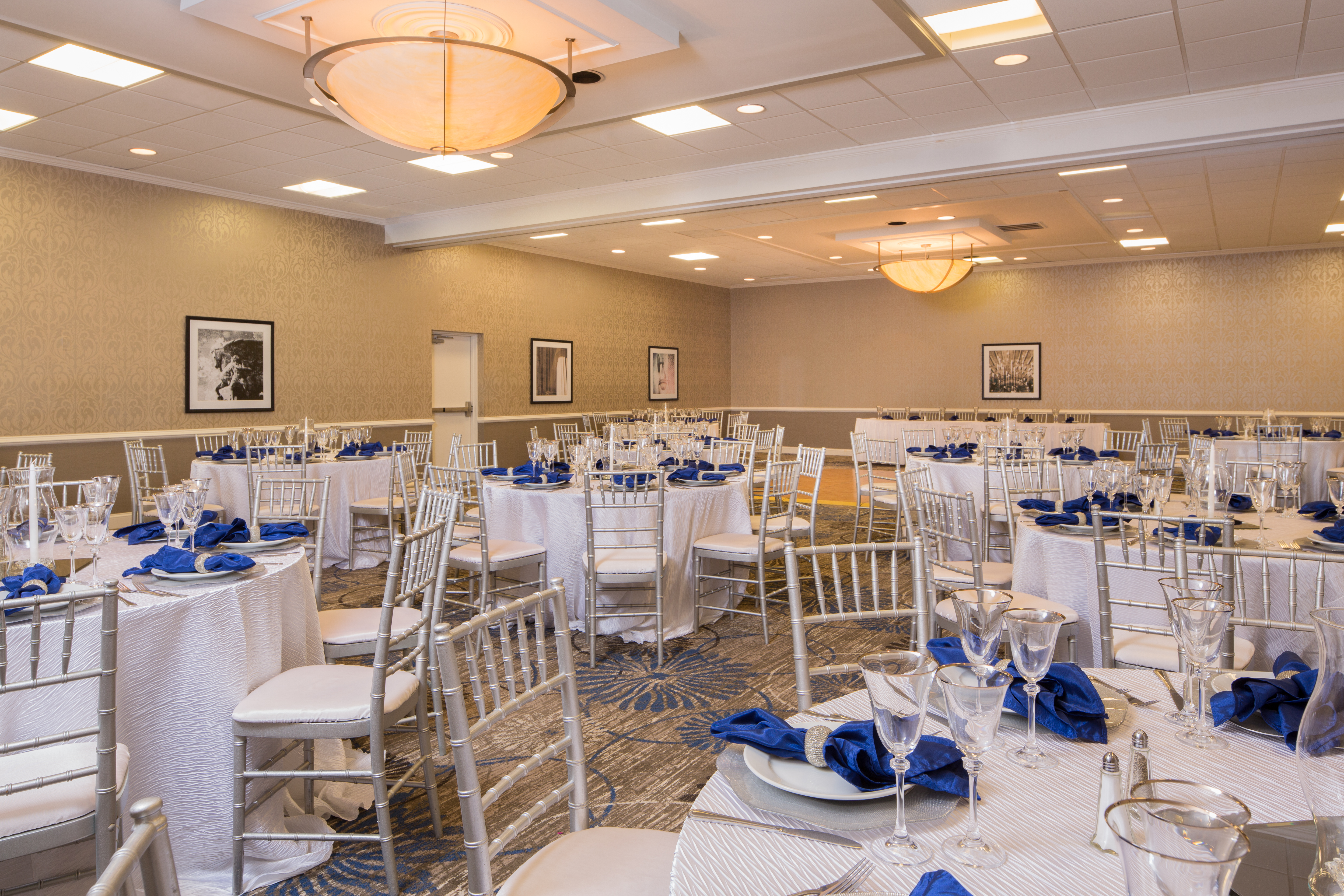 Banquet Setup in Meeting Room With Place Settings and Blue Napkins on Round Tables With White Linens Set Up for a Wedding